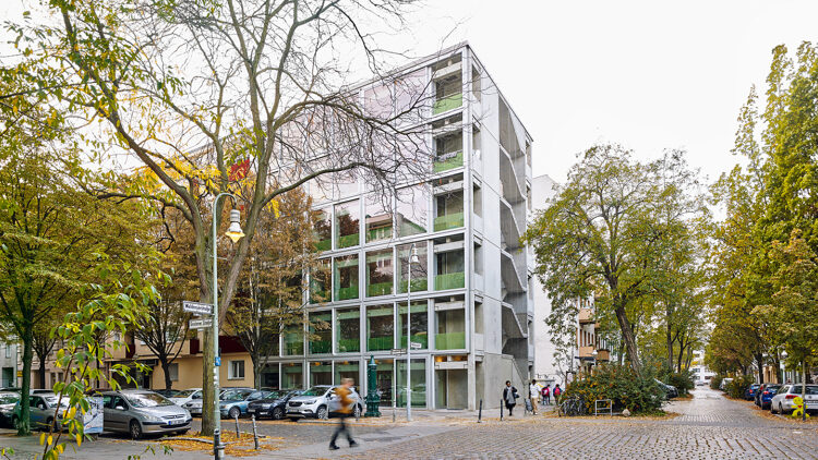 © Tobias Wootton Begrünte Straße mit einem Eckhaus mit Glasfassade