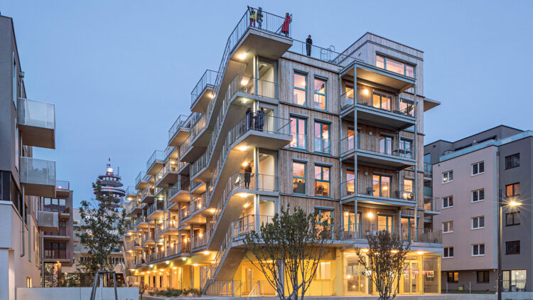 © Hertha Hurnaus Mehrstöckiges Holzhaus in abendlicher Beleuchtung