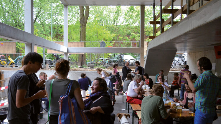 © ifau Mehrere Menschen stehen und sitzen in einem Raum und unterhalten sich