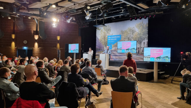 © IBA Hamburg / Daniela Hoffmann Ein Publikum hört zwei Redner:innen auf einer Bühne zu