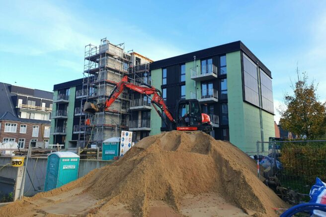 © IBA Hamburg / Arne von Maydell teilweise eingerüstetes, mehrgeschossiges Haus, davon ein großer Sandberg, darauf steht ein Bagger