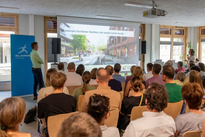 © IBA Hamburg / Bente Stachowske sitzendes Publikum von hinten vor einer Präsentationsleinwand