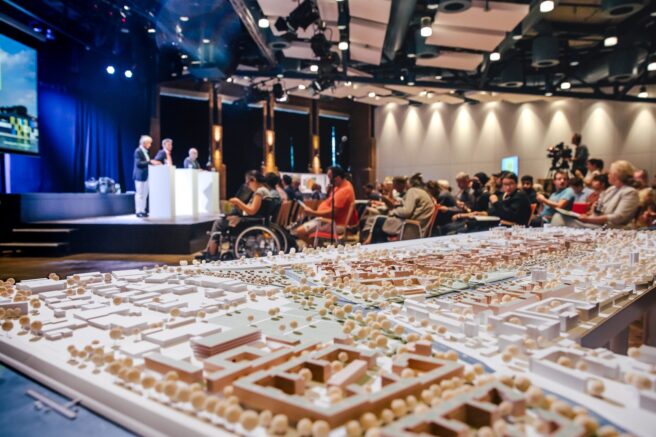 © IBA Hamburg / Christina Clasen Publikum und Redner beim Projektdialog, im Vordergrund das Holzmodell con Wilhelmsburg.