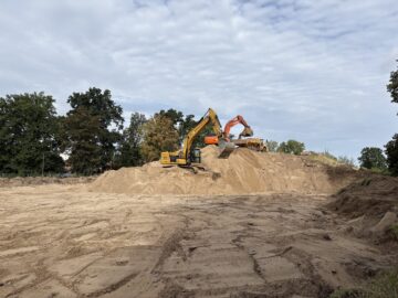 © IBA Hamburg / Jakub Oblocki Ein gelber und ein orangefarbener Bagger arbeiten auf einem großen Sandhügel. Ein Bagger nimmt Sand mit seiner Schaufel auf, während ein Dumper dahinter bereitsteht.