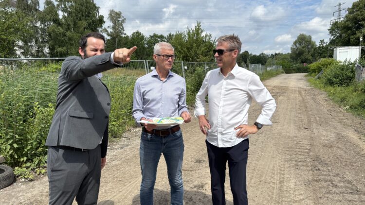 © IBA Hamburg / Arne von Maydell Drei Männer stehen auf einem unbefestigten Weg im Elbinselquartier, einer zeigt mit ausgestrecktem Arm in die Ferne, ein anderer hält einen Lageplan in der Hand