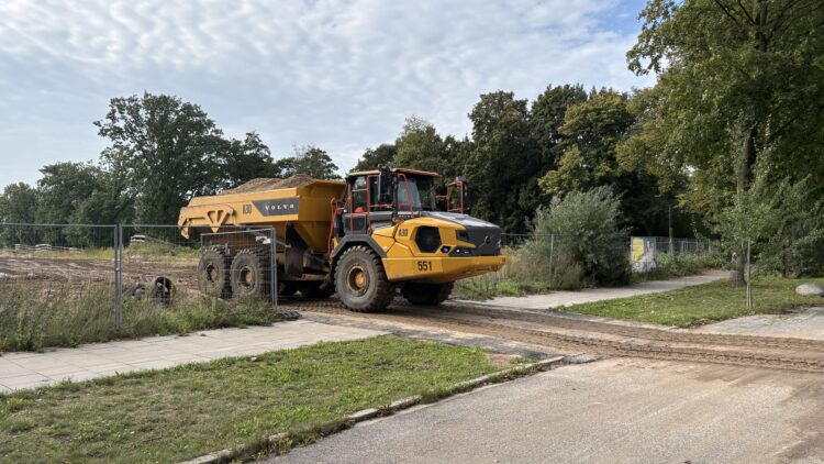 © IBA Hamburg / Jakub Oblocki Ein mit Sand beladener gelber Dumper fährt von der Baustelle des Wilhelmsburger Rathausviertels auf die Rotenhäuser Straße.