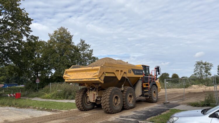 © IBA Hamburg / Jakub Oblocki Ein mit Sand beladener gelber Dumper fährt von der Rotenhäuser Straße auf eine Baustellenzufahrt zum Elbinselquartier.