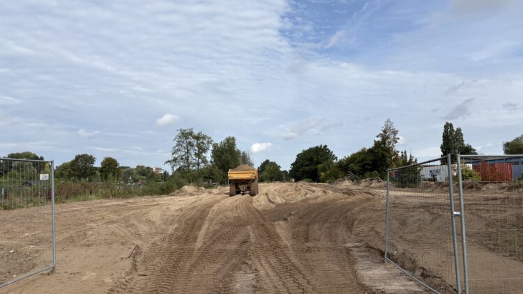 © IBA Hamburg / Jakub Oblocki Ein gelber Dumper fährt über eine sandige Baustellenfläche in Richtung des Nördlichen Elbinselquartiers.
