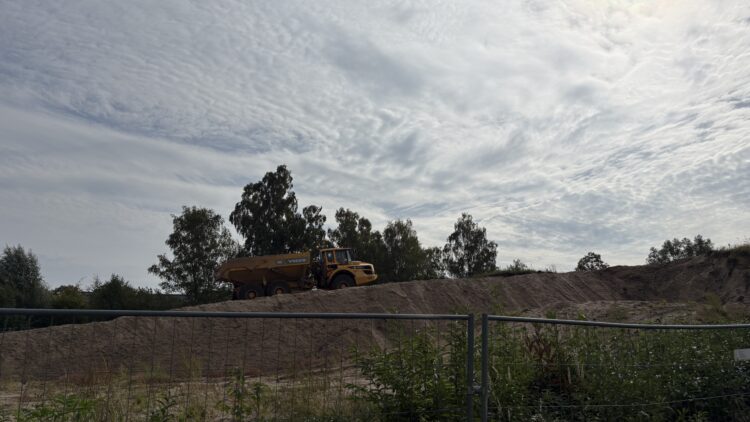 © IBA Hamburg / Jakub Oblocki Ein gelber Dumper fährt einen großen Sandhügel auf einem Damm hinauf. Im Hintergrund sind Bäume und Baustelleneinrichtungen zu sehen.