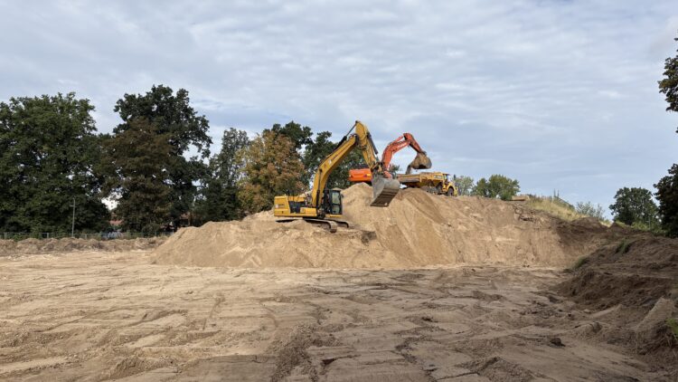 © IBA Hamburg / Jakub Oblocki Ein gelber und ein orangefarbener Bagger arbeiten auf einem großen Sandhügel. Ein Bagger nimmt Sand mit seiner Schaufel auf, während ein Dumper dahinter bereitsteht.