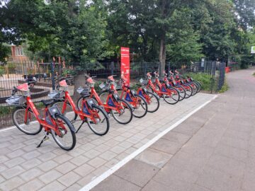 © IBA Hamburg / Deutsche Bahn Connect GmbH Mehrere rote StadtRAD-Fahrräder stehen an der neu eröffneten StadtRAD-Station „Niedergeorgswerder Deich / Rahmwerder Straße“. Im Hintergrund sind ein Spielplatz und die Bushaltestelle zu sehen.