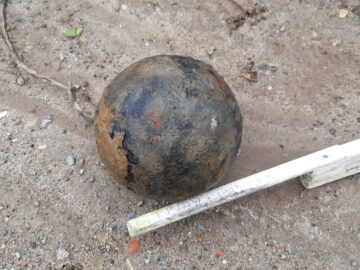 © IBA Hamburg / Thomas Waldau Metallisch wirkende Kugel mit Rostspuren auf sandigem Boden; daneben ein Zollstock zur Größenbestimmung.