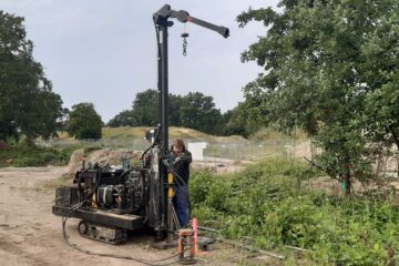 © IBA Hamburg / Thomas Waldau Bohrgerät auf Kettenfahrwerk bei Baugrunduntersuchung, bedient von einer Person; im Hintergrund Bäume und ein Bauzaun.