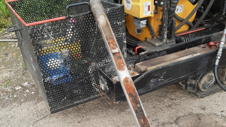 © IBA Hamburg / Thomas Waldau Bohrkern liegt auf sandigem Boden vor gelbem Bohrgerät; daneben ein Metallkorb mit Werkzeugen, im Hintergrund etwas Grün.
