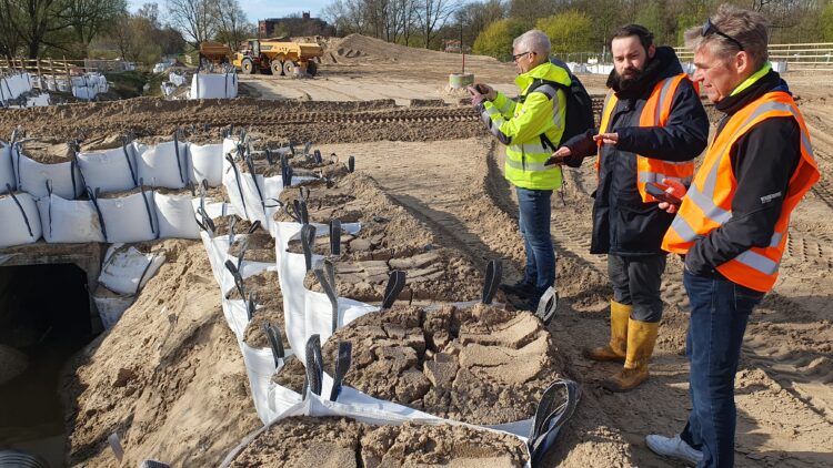 © IBA Hamburg / Arne von Maydell Der IBA-Geschäftsführer sowie zwei IBA-Kollegen stehen in Warnwesten auf der Baustelle und man sieht gefüllte Big Bags.