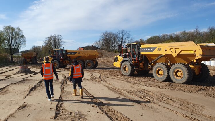 © IBA Hamburg / Arne von Maydell Zwei IBA-Mitarbeitende gehen über die sandige Baustelle mit Baufahrzeugen im Hintergrund.