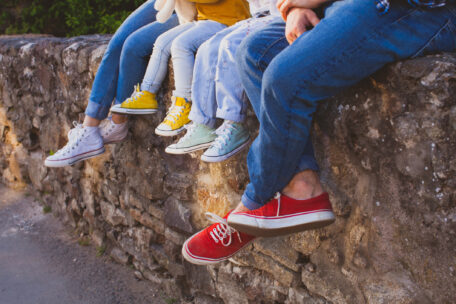 © oksix Eine Gruppe Menschen sitzt auf einer Mauer, zu sehen sind hauptsächlich die Beine