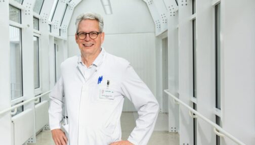 © IBA Hamburg / Katja Ruge Prof. Müller steht in einem hellen Gang und lächelt zur Kamera.