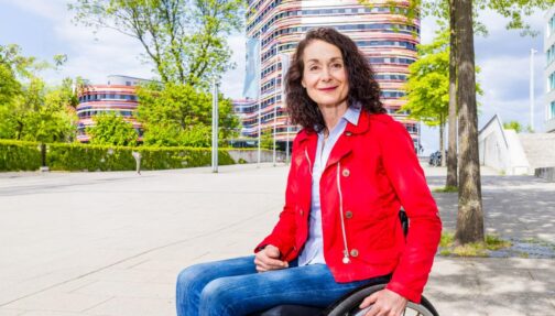 © IBA Hamburg / Katja Ruge Sylvia Pille-Steppat sitzt in ihrem Rollstuhl mit Bürogebäuden im Hintergrund.