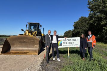 © IBA Hamburg / Arne von Maydell Christian Carstensen, Kay Gätgens, Karen Pein, René Herrmann stehen um ein Schild mit der Aufschrift "Fischbeker Reethen", im Hintergrund eine große Baumaschine und Ackerland