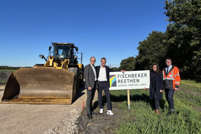 © IBA Hamburg / Arne von Maydell Christian Carstensen, Kay Gätgens, Karen Pein, René Herrmann stehen um ein Schild mit der Aufschrift "Fischbeker Reethen", im Hintergrund eine große Baumaschine und Ackerland