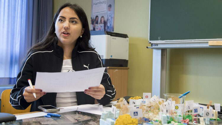 Eine Schülerin sitzt vor einem gebastelten Modell und redet