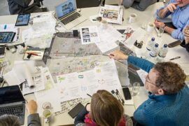 Menschen sitzen um einen Tisch, auf dem Pläne und Zeichnungen liegen
