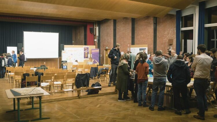 © IBA Hamburg GmbH / Jo Larsson Menschen stehen in einem Raum um einen Tisch