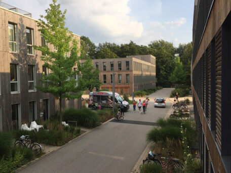 © Patrick Bauer Blick aus einem Fenster auf eine Straße mit umliegender Bebauung mit Holzfassade