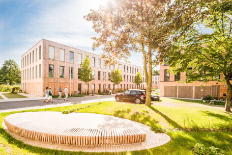 © IBA Hamburg GmbH / Johannes Arlt Vier Menschen laufen an einem Mehrfamilienhaus mit Holzfassade vorbei